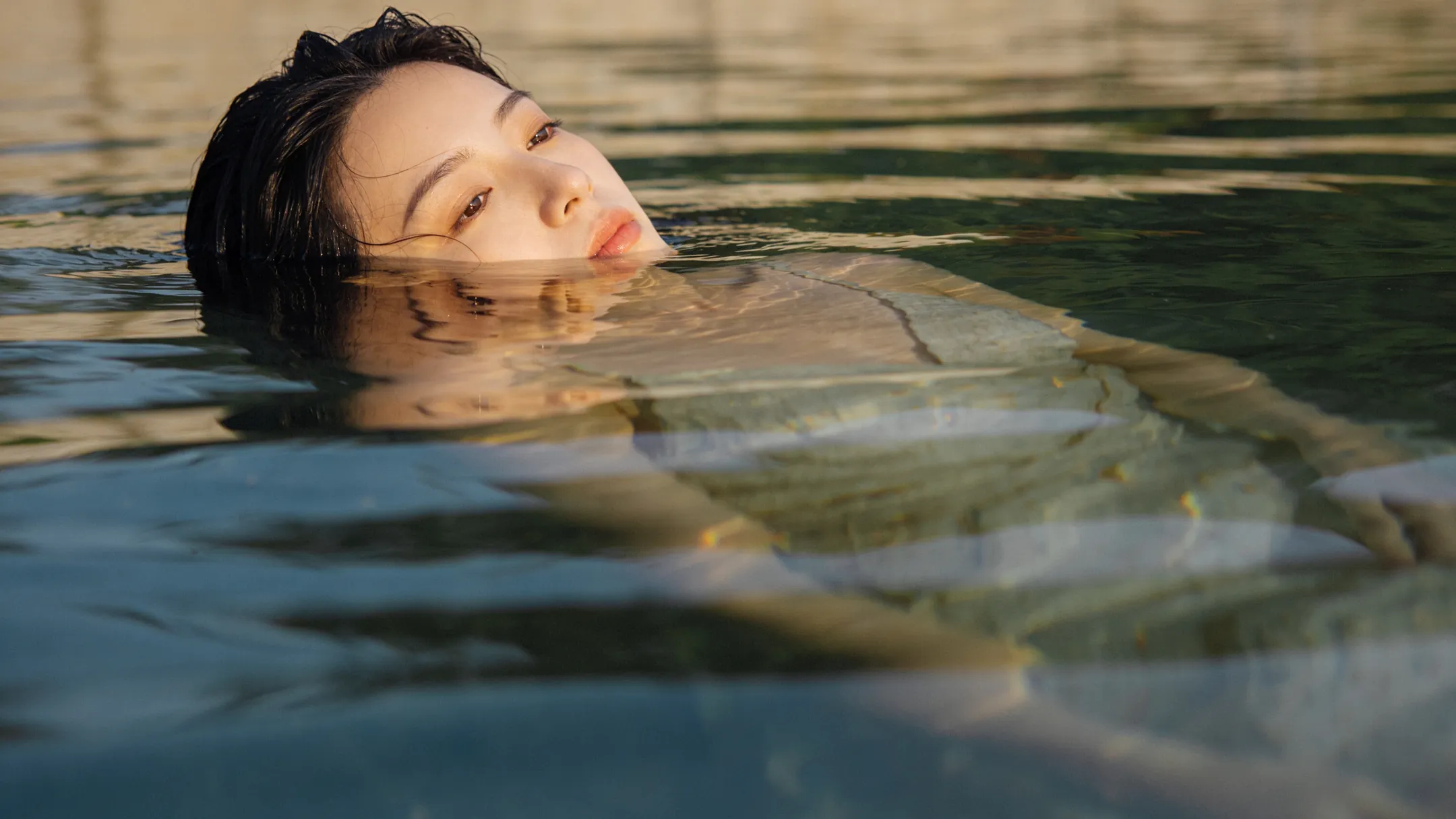 Woman half-submerged, face reflected, soft poetic tones.