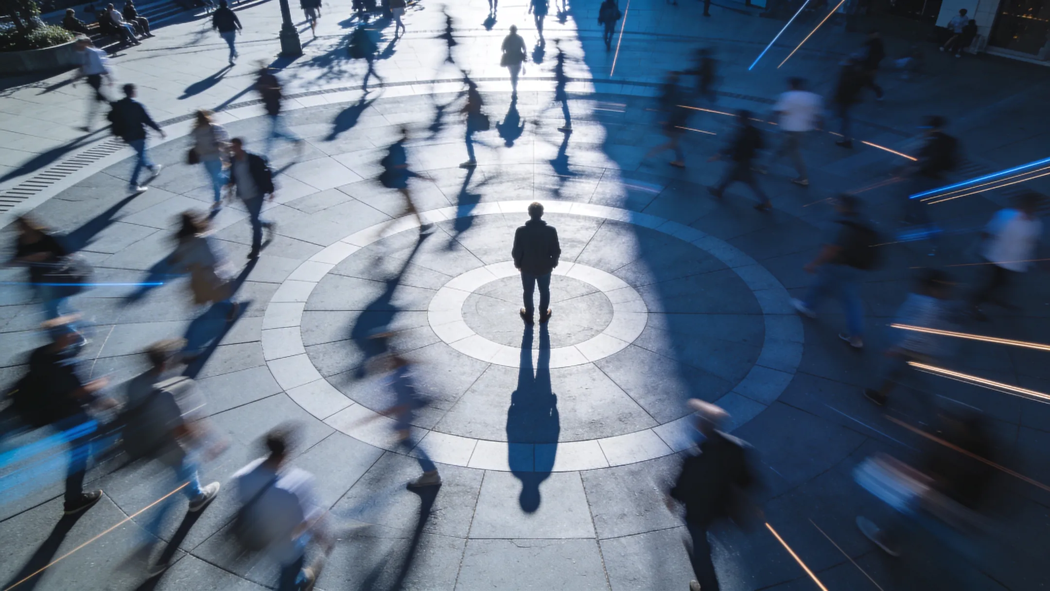 Person stands still as blurred crowds rush by, long exposure effect.