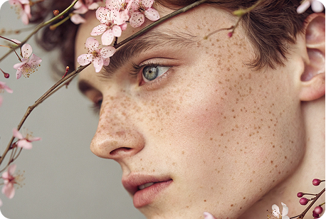 Gentle freckled man with pink floral face art, serene.